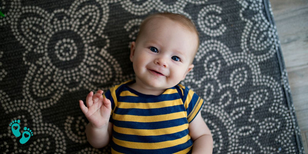 Happy baby wearing striped onesie on patterned rug, perfect fit for Grookz baby shoes