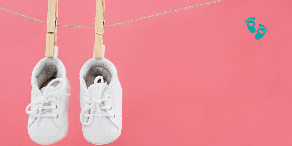 White Grookz baby sock shoes hanging on a clothesline against a pink background, demonstrating how to clean baby sock shoes.