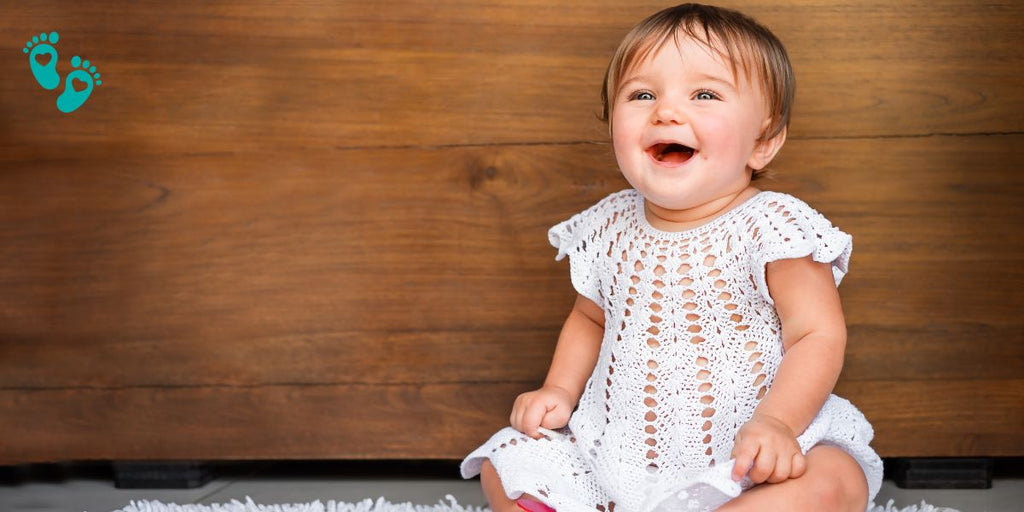 Happy baby in a white crocheted outfit sitting on a rug, illustrating the comfort and cuteness of Grookz baby shoes