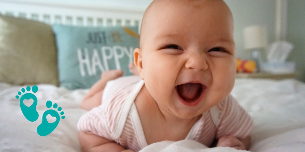 Smiling baby lying on a bed, providing a guide on where to buy baby's first shoes with insights from Grookz Shoes