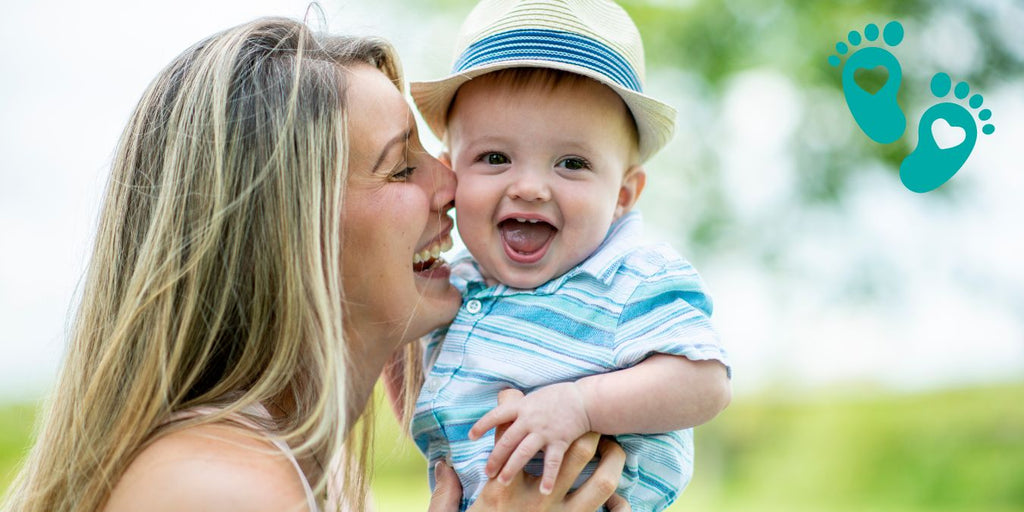 Happy mother holding her smiling baby boy in a hat, highlighting Grookz Shoes guiding your baby's first adventures from crawling to walking