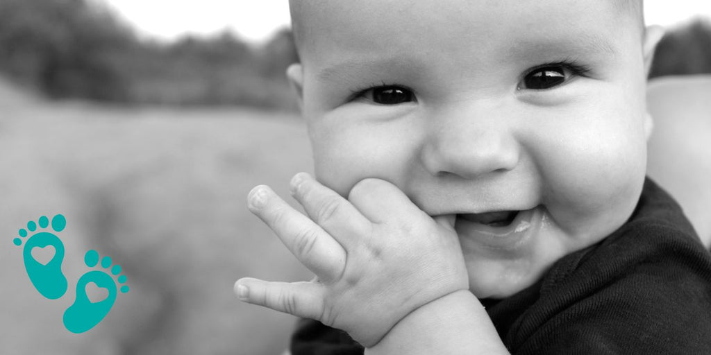 Happy baby smiling and touching their face, promoting the benefits of investing in high-quality Grookz baby shoes