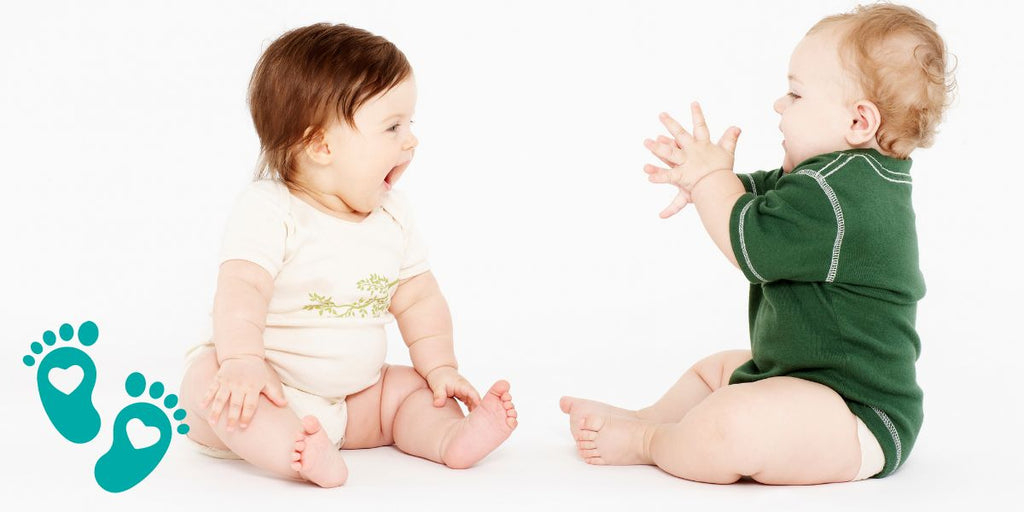 Two babies sitting and interacting, unraveling the mystery of whether baby shoes help with walking, with insights from Grookz Shoes