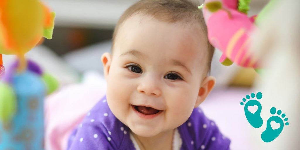 Smiling baby in a purple outfit surrounded by toys, discussing what size baby shoes your baby needs with Grookz Shoes