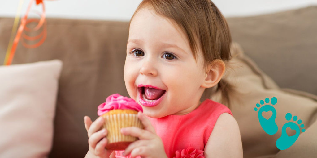 Happy toddler eating a cupcake, discussing when babies should start wearing shoes with a guide to Grookz Shoes