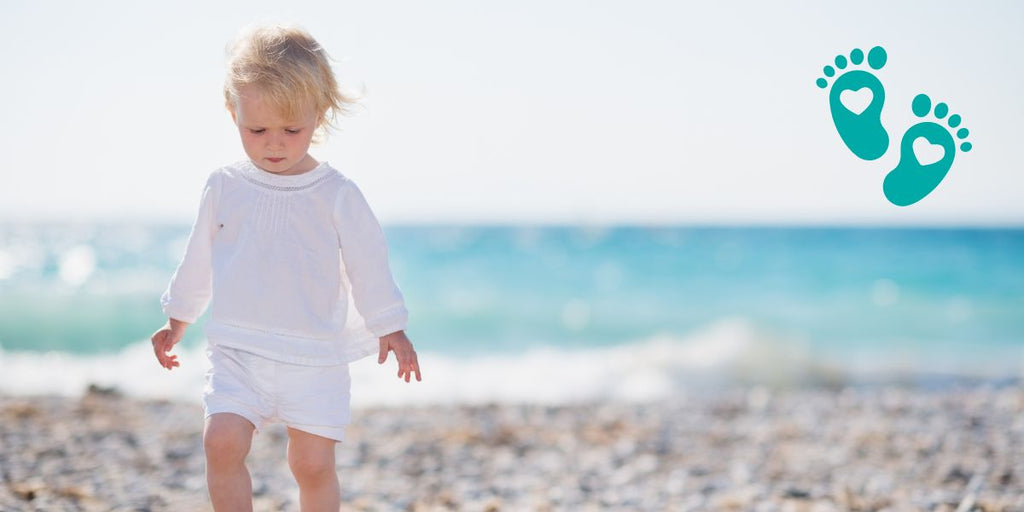 Toddler walking on a beach in white clothing, emphasizing the importance of non-slip sock shoes from Grookz for safety and comfort