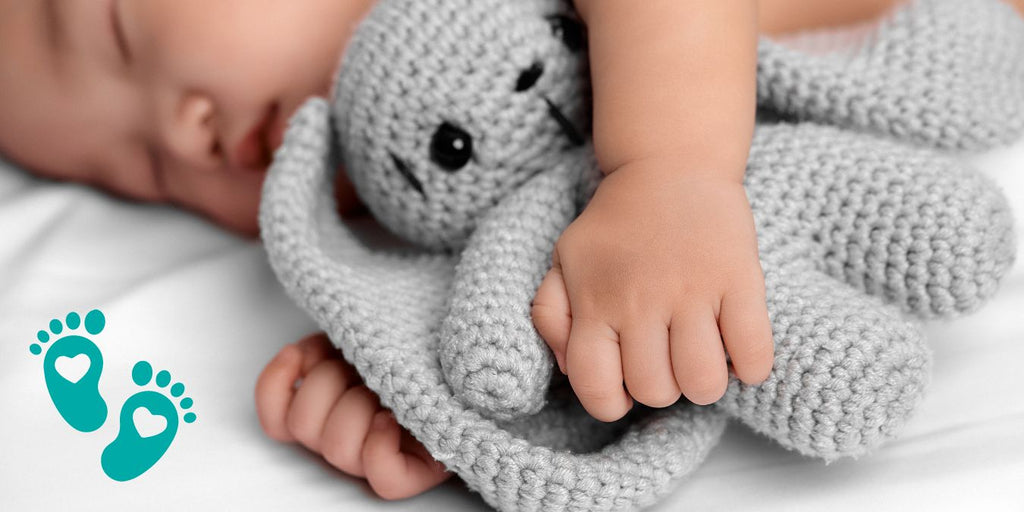 Sleeping baby holding a knitted toy, discussing what babies should be doing at 9 months and how baby shoes from Grookz play a role